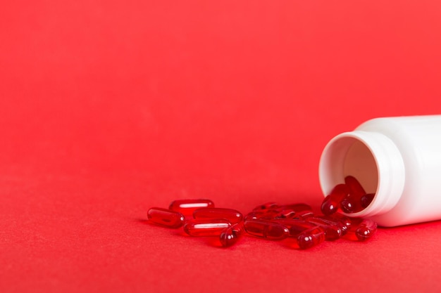 Pílulas vermelhas derramadas em torno de um frasco de comprimidos Medicamentos e pílulas de prescrição Fundo plano Cápsulas médicas vermelhas