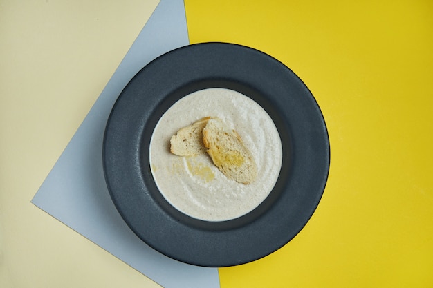Pilzcremesuppe mit Champignons, garniert mit Crutons in einer weißen Schüssel auf einer farbigen Oberfläche. Gesunde Ernährung. Draufsicht Essen