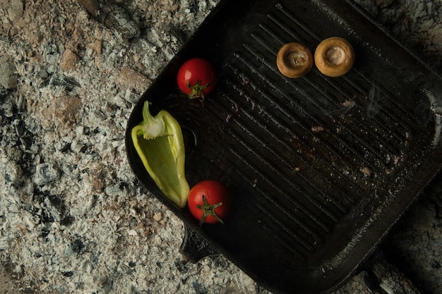 Pilze mit Tomaten auf einem Backblech liegen auf Holzkohle. das Gericht wird auf Holzkohle gekocht und geräuchert