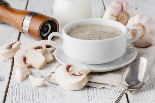 Pilzsuppe im weißen Topf auf weißem Holz