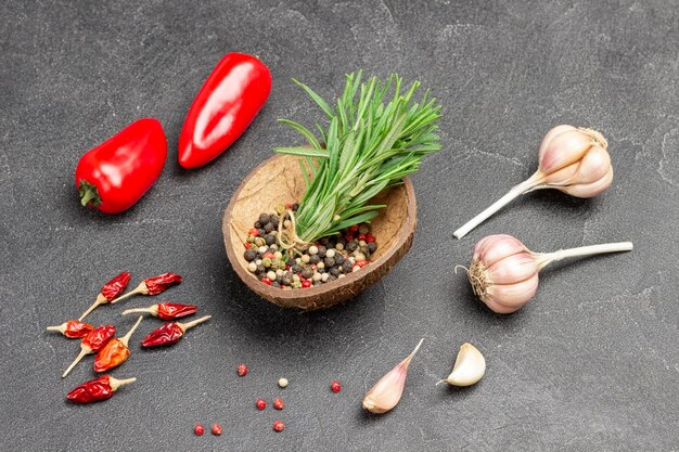 Piment und Rosmarinzweige in einer Kokosnussschale. Trockene Paprikaschoten, frische Paprika und Knoblauch. Schwarzer Hintergrund. Ansicht von oben