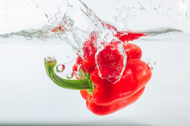 Pimenta doce em salpicos de água, pimentão vermelho sobre branco