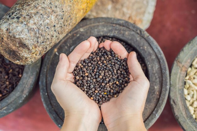 Pimenta preta nas mãos femininas em um fundo de especiarias.