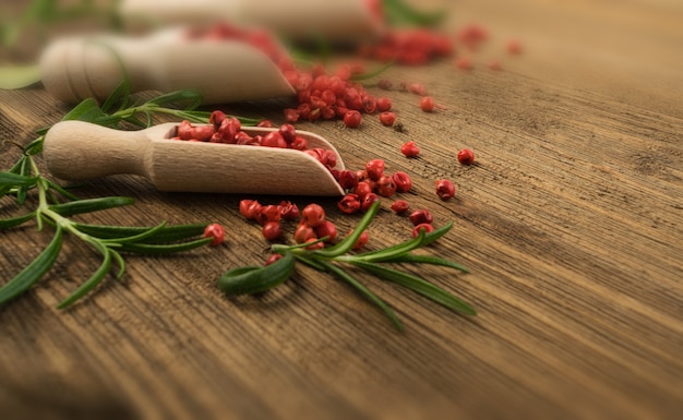 Pimenta rosa ou grãos de pimenta vermelha na mesa de madeira. sementes secas de schinus com alecrim fresco em mesa rústica de madeira