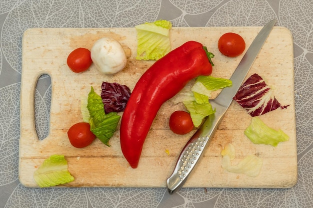 Pimenta vermelha com faca e legumes na tábua de madeira