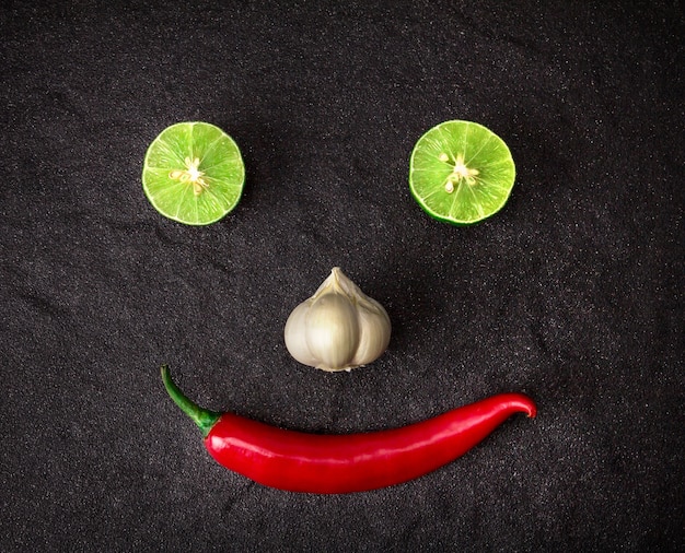 pimentão vermelho, alho e limão limão organizar como rosto sorridente em fundo preto de pedra