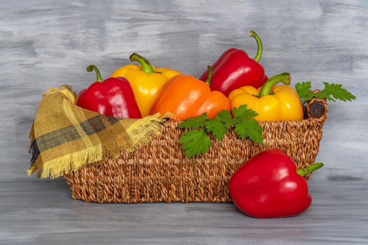 Foto pimentas frescas, amarelas e vermelhas com salsa, em uma cesta de bambu, sobre um fundo de papel cinza.