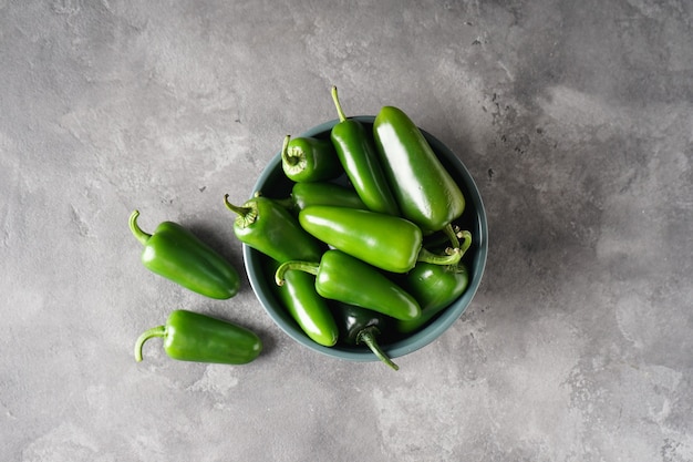 Pimentas jalapeno verdes em um prato sobre um fundo cinza, vista superior.