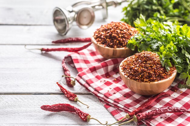 Pimentas secas e trituradas em tigelas de madeira com ervas de salsa.