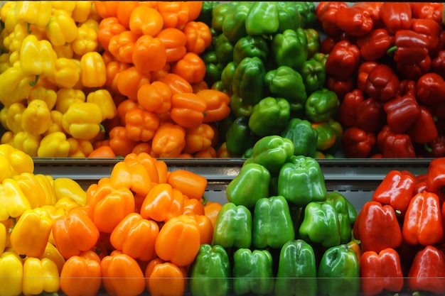 Pimentas vegetais vermelhas, amarelas, laranja e verdes na prateleira da loja com reflexo no espelho