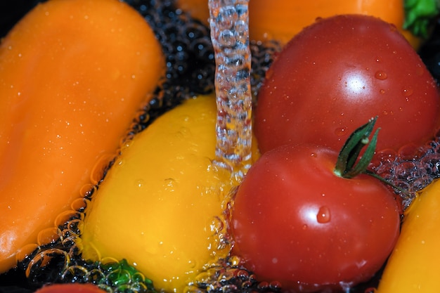 Pimentões multicoloridos e tomates vermelhos maduros são lavados em macro fotografia de água limpa em um fundo preto