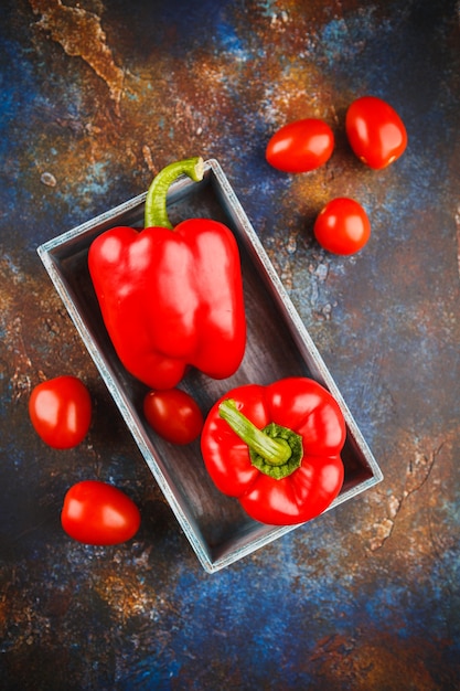 Pimentões vermelhos em uma caixa de madeira e tomates em preto. Vista do topo.