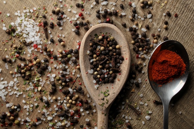 Foto pimienta negra, guisantes, sal marina, pimiento rojo, especias en polvo en una cuchara sobre un fondo de madera