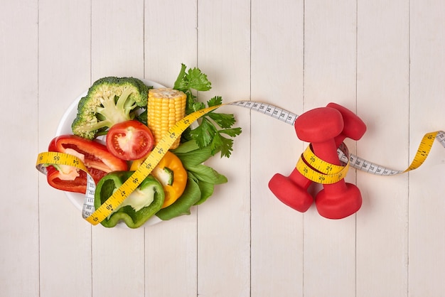 Pimiento con cinta métrica, pesas y botella de agua, aislado en blanco