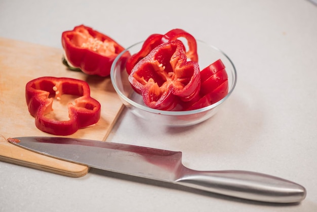 Pimiento dulce rojo fresco en una tabla de madera y en un recipiente de vidrio cerca del cuchillo