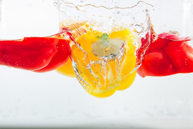 Foto pimiento dulce en las salpicaduras de agua amarillas, rojas y verdes, pimiento dulce en blanco