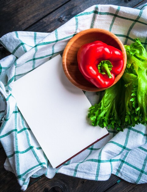 Pimiento rojo maduro en un tazón de bambú, lechuga y cuaderno