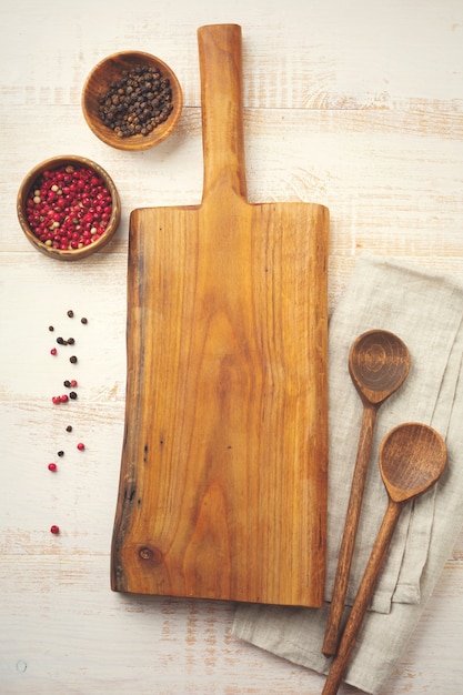 Pimiento rojo y negro, hojas de albahaca, cacerola de cerámica, soporte de madera, cucharas viejas y sencillas y servilleta de lino a la luz. Concepto de accesorios de cocina.