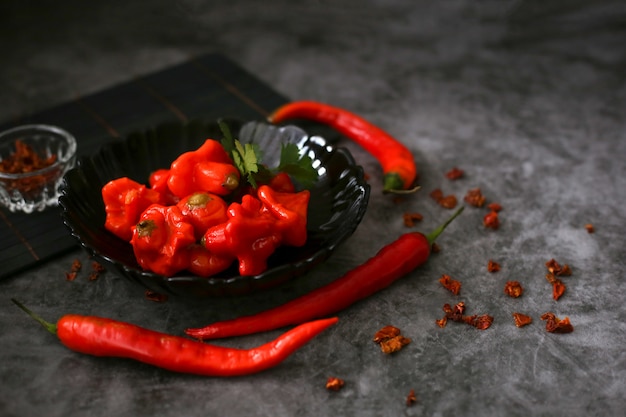 Foto pimiento rojo picante fermentado en un plato negro junto al pimiento rojo picante largo y fresco sobre una superficie gris