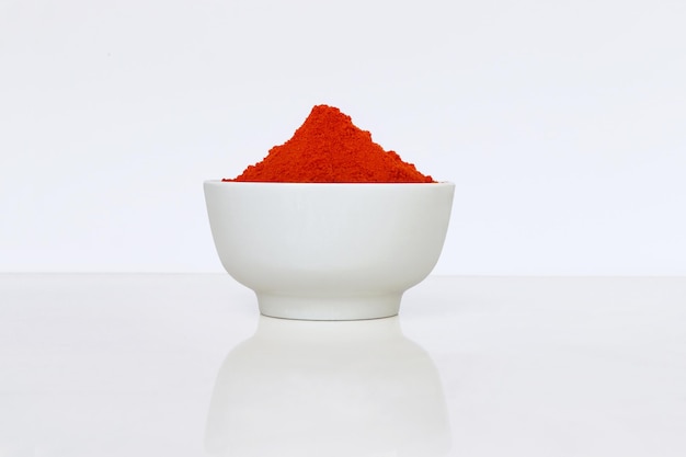 Pimiento rojo seco en polvo en un recipiente blanco sobre fondo blanco.