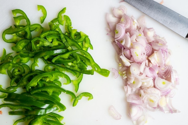 Pimiento verde cortado a lo largo y cebolla picada en una tabla de cortar blanca Preparación para cocinar Antecedentes alimentarios El concepto de vegetarianismo alimentación saludable