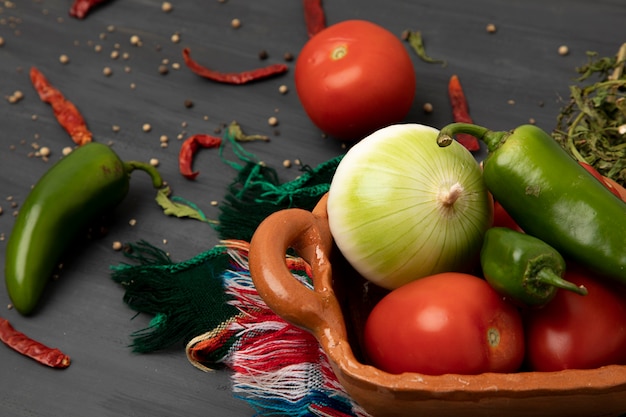 Pimientos, cebolla y pimiento en un recipiente de arcilla sobre una mesa gris