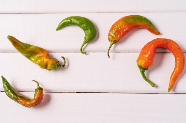 Pimientos doblados curvados feos de moda en el fondo de madera blanco.