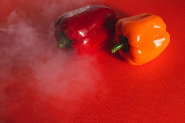 Foto pimientos dulces rojos y naranjas sobre fondo rojo con un ligero humo