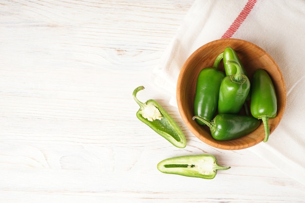 Pimientos jalapeños verdes en una placa de madera sobre un fondo de madera, lugar para el texto, vista superior.