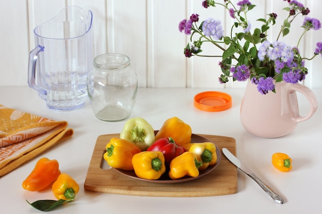 Foto pimientos maduros y un ramo de ageratum en una jarra de flores y verduras sobre una mesa blanca