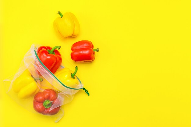 Pimientos rojos y amarillos maduros frescos en bolsas de malla ecológicas reutilizables en el amarillo.