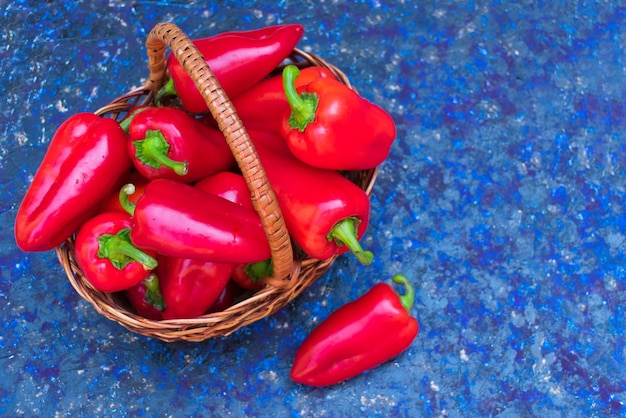 Pimientos rojos (dulces) en una cesta de mimbre sobre un fondo azul. Copie el espacio Vista superior.