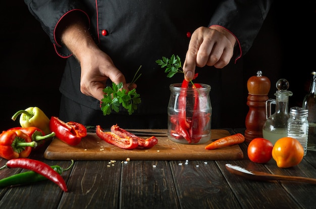 Pimientos rojos dulces en rodajas en una tabla de corte de madera un chef profesional con un uniforme negro prepara una ensalada una mano de hombre pone perejil en un frasco