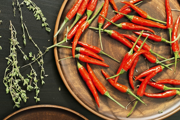 Pimientos rojos picantes y tomillo de limón en un plato plano casero de arcilla marrón. Vista superior e iluminación discreta.