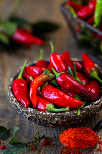 Pimientos rojos con una ramita de albahaca en una cesta de metal de mimbre sobre una mesa de madera.