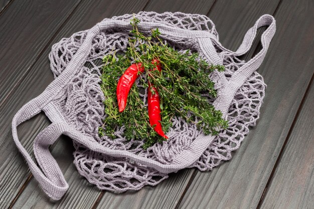 Pimientos rojos y ramitas de tomillo en bolsa de malla de algodón natural reutilizable. Concepto de desperdicio cero. Vista superior