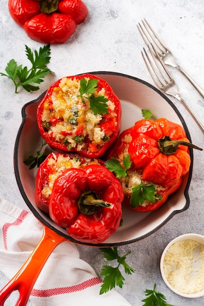 Pimientos rojos rellenos de arroz y verduras en sartén de hierro fundido sobre fondo de hormigón gris