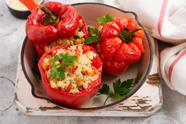 Pimientos rojos rellenos de arroz y verduras en sartén de hierro fundido sobre fondo de hormigón gris.