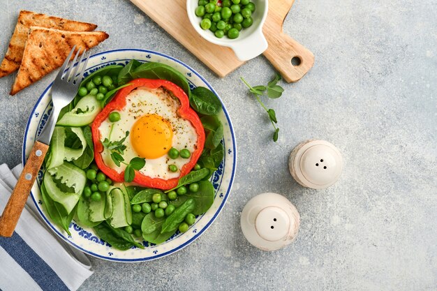 Pimientos rojos rellenos de huevos, hojas de espinaca, guisantes y microgreens en un plato de desayuno sobre fondo gris claro. Vista superior.