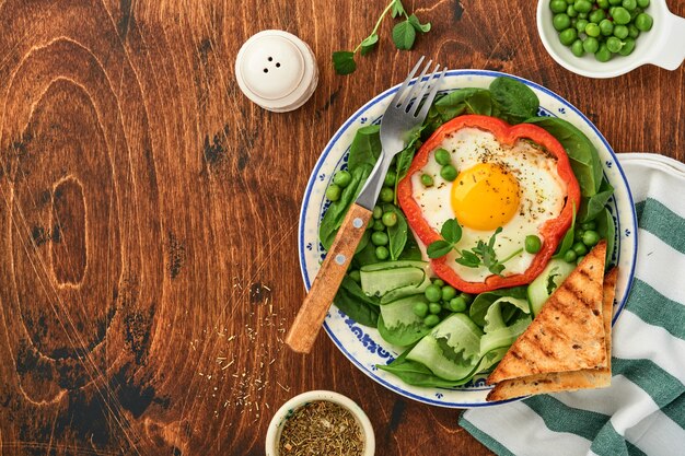 Pimientos rojos rellenos de huevos, hojas de espinaca, guisantes y microgreens en un plato de desayuno sobre fondo de mesa de madera vieja. Vista superior.