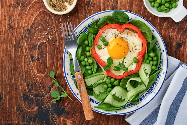 Pimientos rojos rellenos de huevos, hojas de espinaca, guisantes y microgreens en un plato de desayuno sobre fondo de mesa de madera vieja. Vista superior.