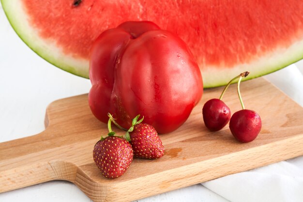 Pimientos rojos, sandía, cerezas y fresas en el fondo y el tejido de mesa blanca