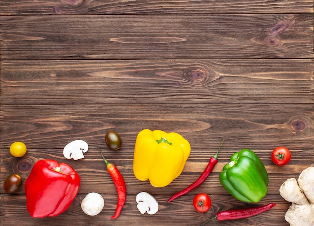 Pimientos rojos, verdes y amarillos, setas y tomates cherry sobre fondo de madera