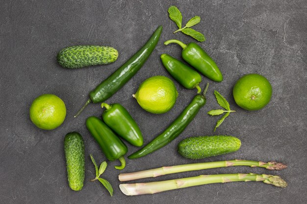 Pimientos verdes, espárragos, pepinos y limas en la mesa. Fondo negro. Endecha plana