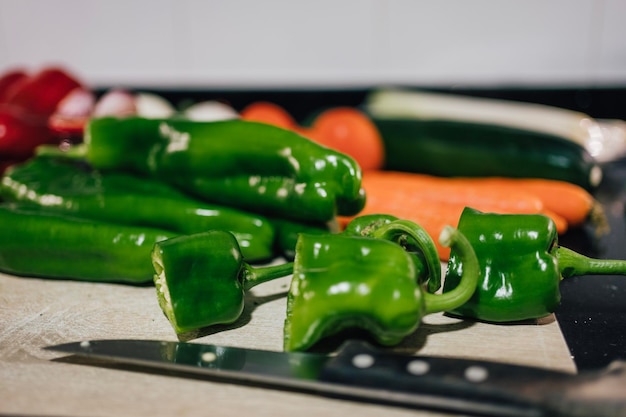 Pimientos verdes italianos cortados en una tabla para cortar con un cuchillo de chef Verduras rojas y blancas anaranjadas en el fondo