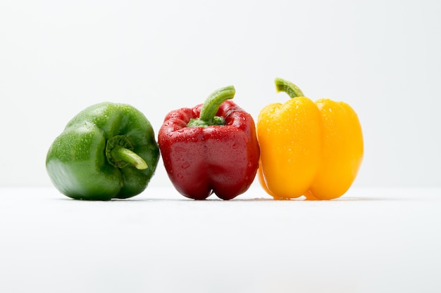 Pimientos verdes, rojos y amarillos en la mesa blanca y blanca.