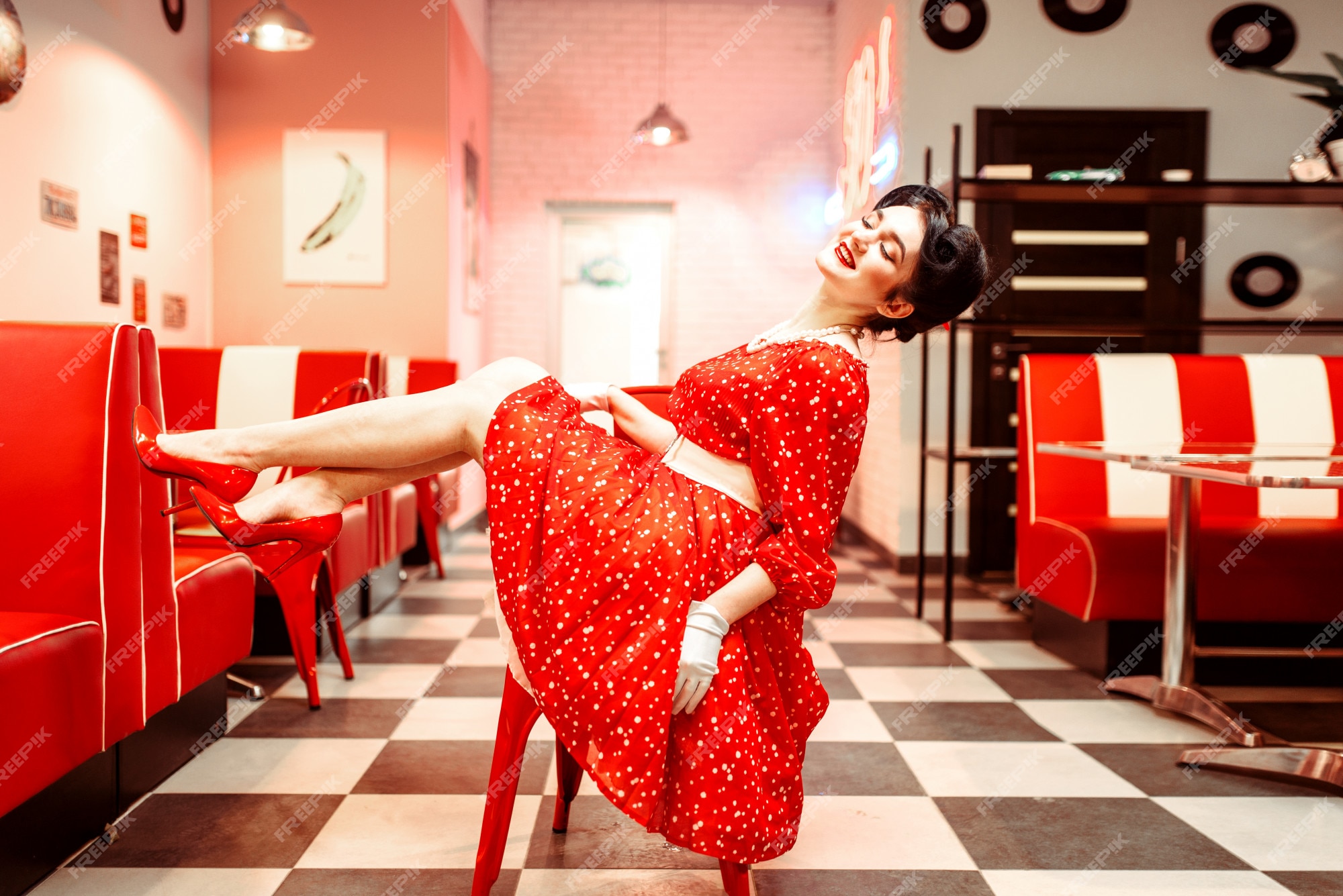 Pin up girl con maquillaje posando en la silla en retro cafe, 50 american fashion. zapatos rojos vestido con lunares, estilo vintage | Foto Premium