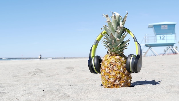 Piña en auriculares, playa de arena, costa de California. Torre de frutas y salvavidas de Ananas.