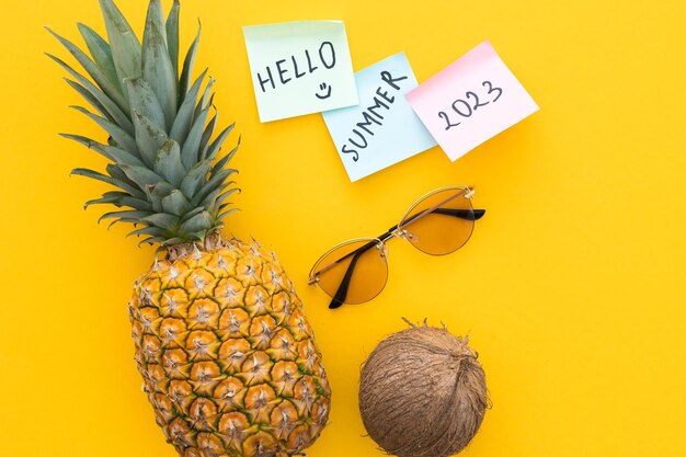 Piña y coco y gafas de sol sobre un fondo amarillo brillante Palabra hola verano 2023