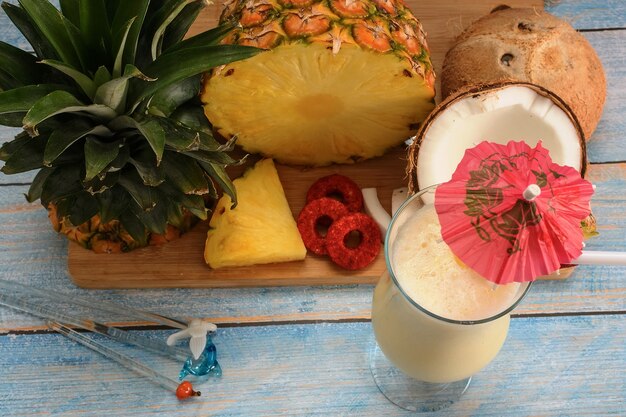 Piña colada con frutas frescas en la tabla de cortar de madera en la mesa de la pizarra blanca y fondo azul.